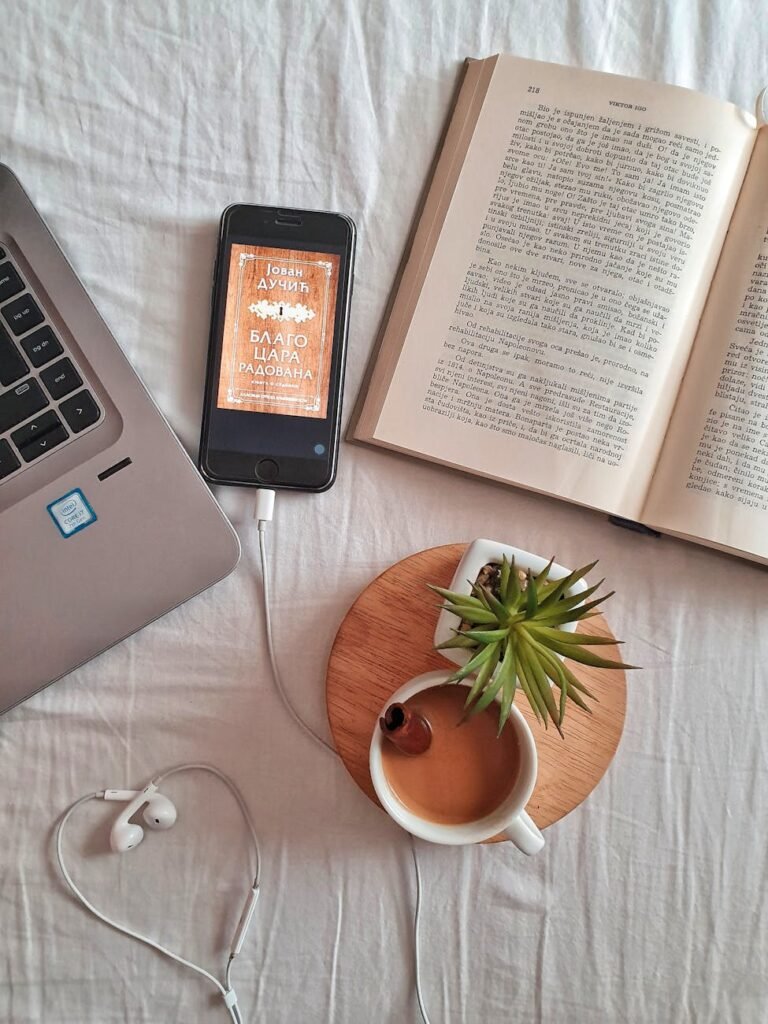 Relaxing workspace flat lay featuring a laptop, book, coffee cup, smartphone, and plant on a white surface.