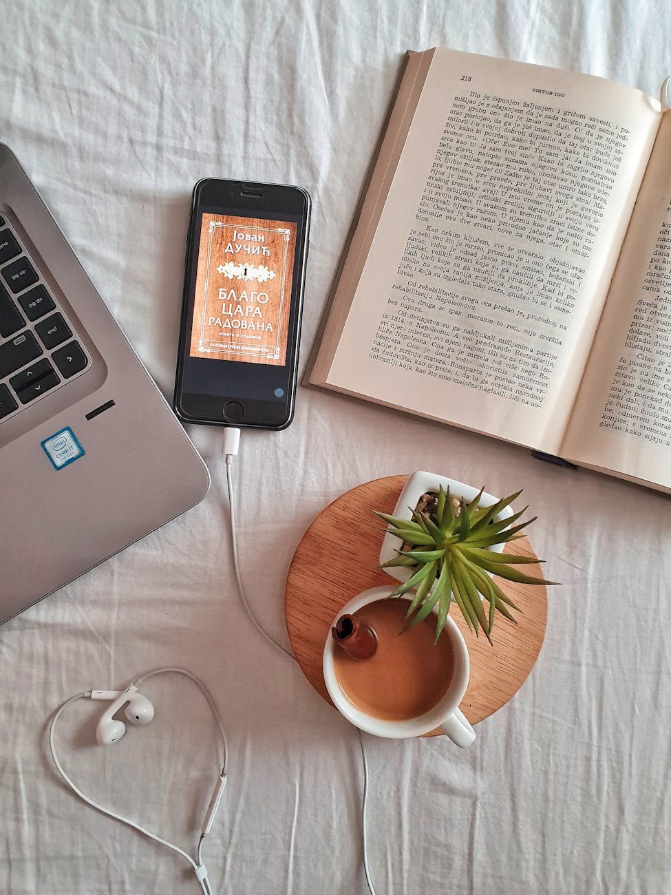 Relaxing workspace flat lay featuring a laptop, book, coffee cup, smartphone, and plant on a white surface.